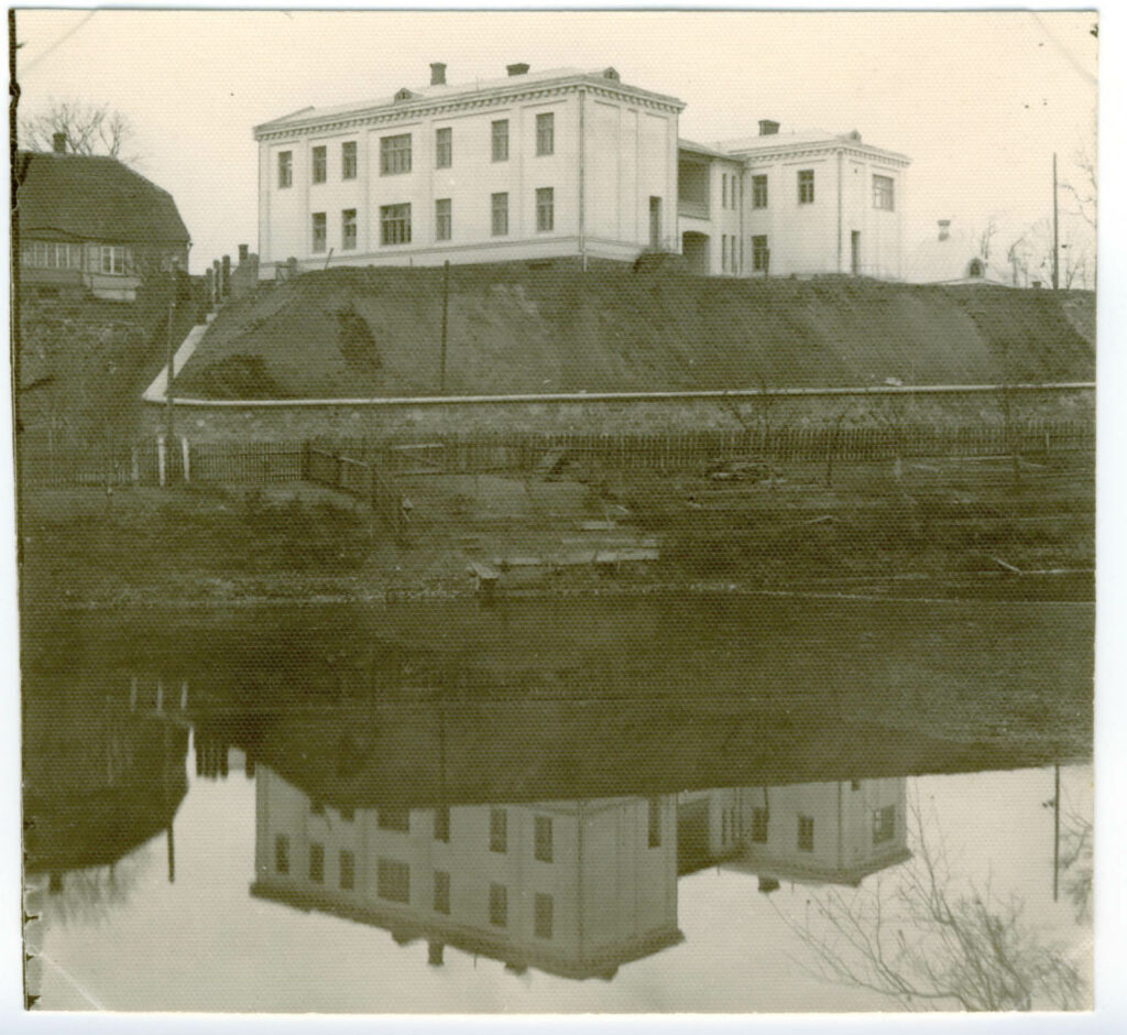 Romantiski. Ēkas atspulgs netālajā Dzirnavu ezeriņā 1914. gada rudenī. Tolaik slimnīcai divi stāvi. Trešo tā ieguva jau krietni vēlāk, pēc Otrā pasaules kara (1959.)