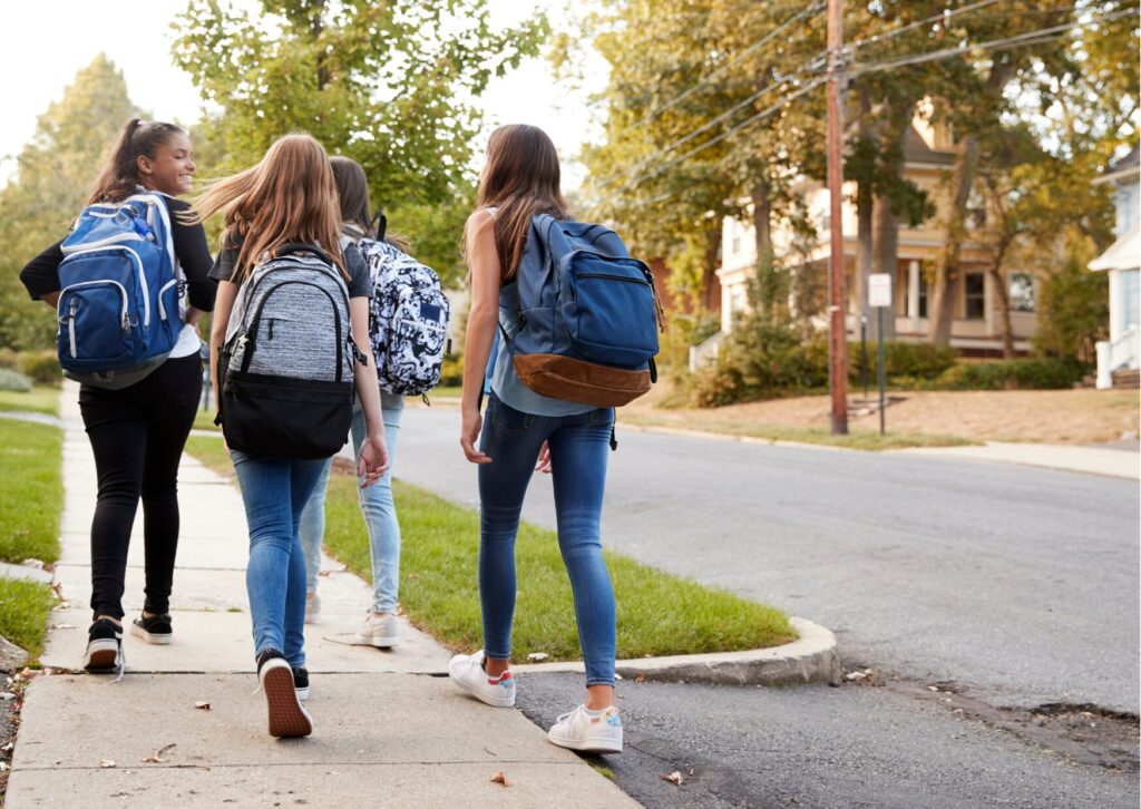 Četras meitenes iet ar skolas somām uz pleciem.