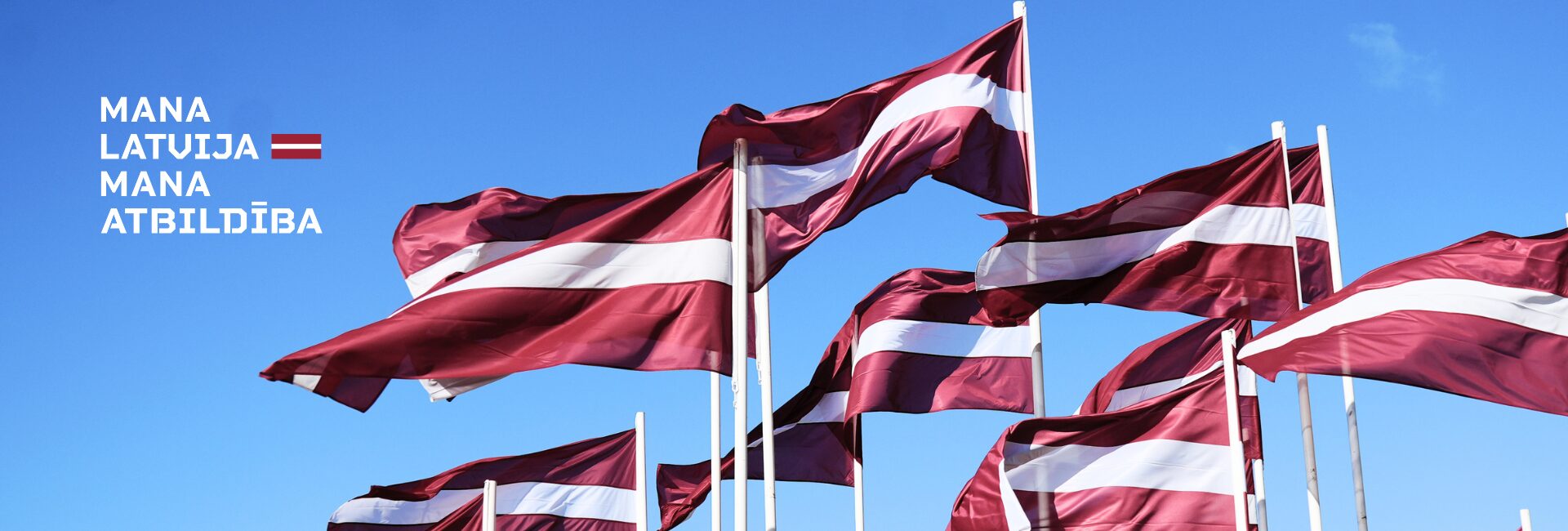 Plīvojoši Latvijas karogi un uzraksts 